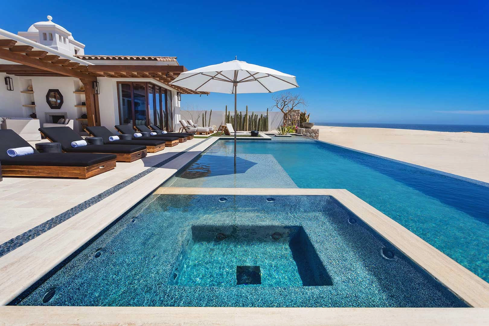 Pool and jacuzzi of a Norman Estates beachside home with the dunes and ocean beyond