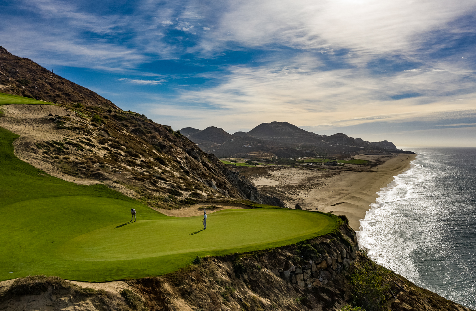 Golfers on the cliffside green of Quivira Golf Club, the Pacific beach and the mountains behind